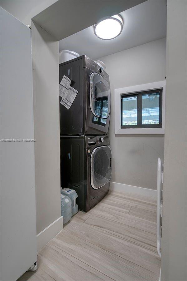 clothes washing area with stacked washer and dryer and light wood-type flooring