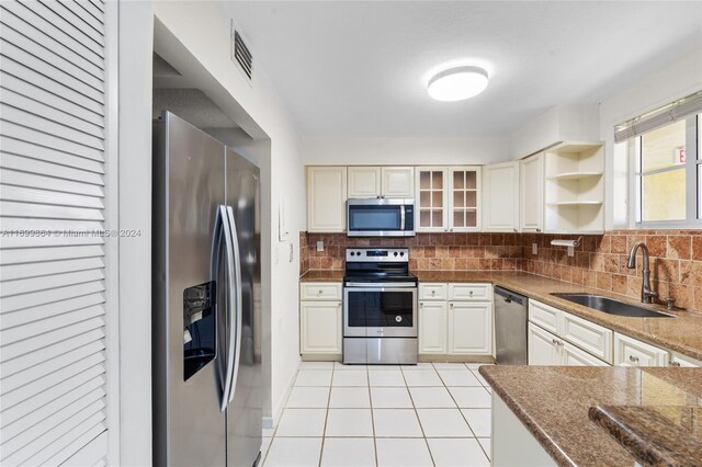 kitchen with sink, stainless steel appliances, tasteful backsplash, dark stone counters, and light tile patterned floors