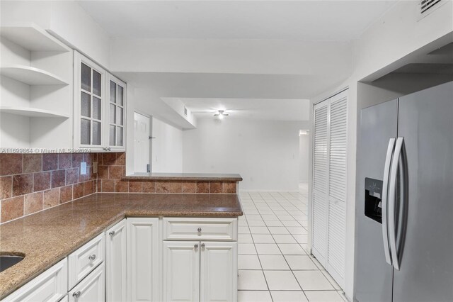 kitchen with light tile patterned flooring, backsplash, stainless steel fridge with ice dispenser, white cabinetry, and kitchen peninsula