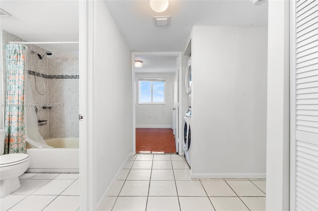 bathroom featuring tile patterned flooring, stacked washing maching and dryer, shower / bath combo, and toilet