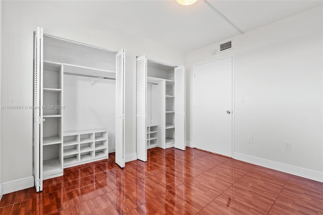 unfurnished bedroom with wood-type flooring and two closets