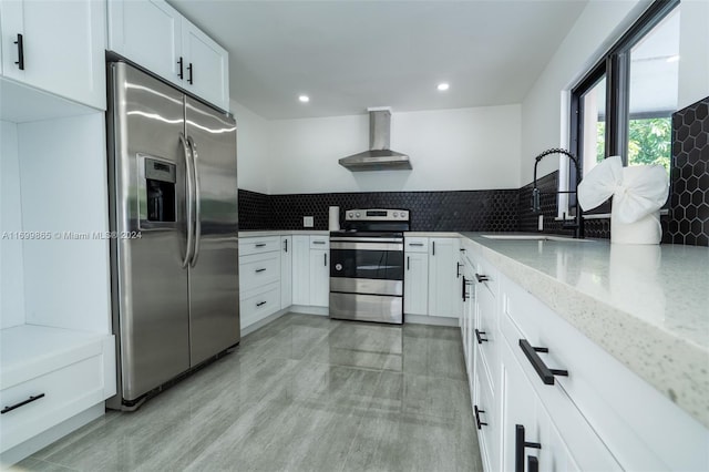 kitchen with white cabinets, wall chimney range hood, sink, decorative backsplash, and stainless steel appliances