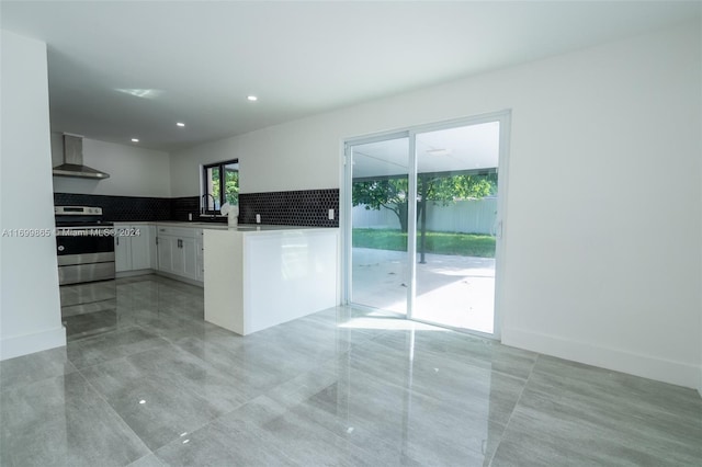 kitchen with wall chimney range hood, backsplash, kitchen peninsula, stainless steel electric range, and white cabinets