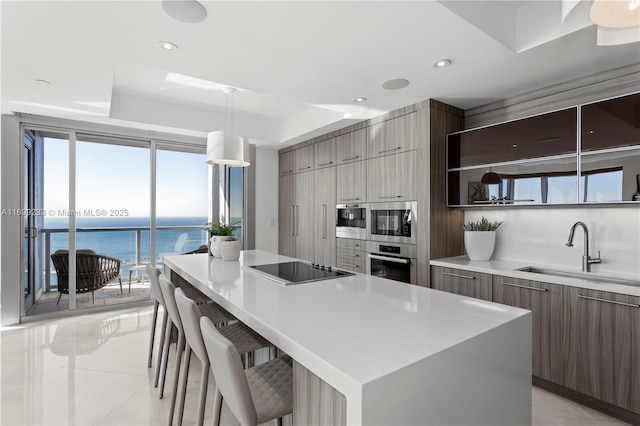 kitchen featuring sink, a kitchen bar, a center island, black electric stovetop, and a water view