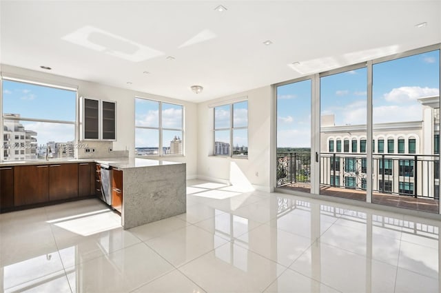 kitchen with floor to ceiling windows, stainless steel dishwasher, kitchen peninsula, decorative backsplash, and light tile patterned floors