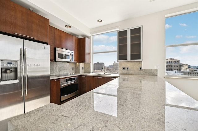 kitchen with backsplash, light stone countertops, sink, and stainless steel appliances