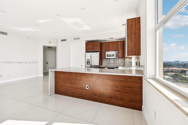 kitchen featuring light stone countertops, sink, stainless steel appliances, kitchen peninsula, and decorative backsplash