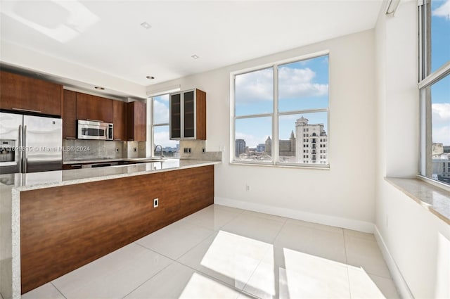 kitchen with light stone countertops, light tile patterned floors, backsplash, and appliances with stainless steel finishes