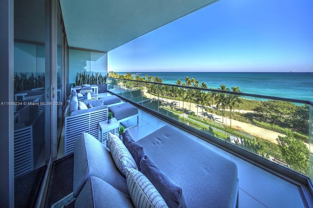 balcony with a view of the beach, an outdoor living space, and a water view