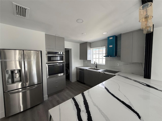 kitchen featuring gray cabinetry, sink, wall chimney exhaust hood, light stone counters, and stainless steel appliances