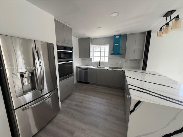 kitchen with gray cabinetry, sink, wall chimney exhaust hood, stainless steel appliances, and hardwood / wood-style floors