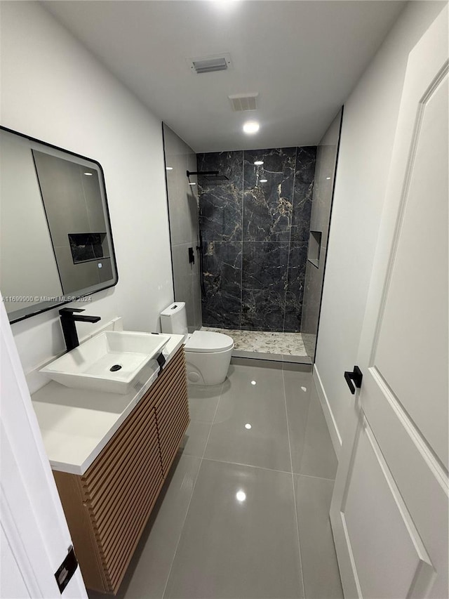 bathroom featuring tile patterned flooring, a tile shower, vanity, and toilet