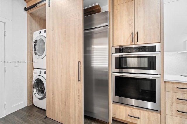 kitchen with appliances with stainless steel finishes, dark hardwood / wood-style flooring, light brown cabinets, a barn door, and stacked washer / drying machine