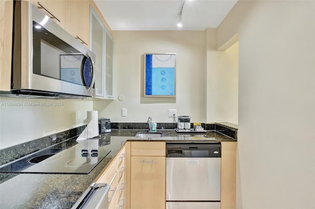 kitchen with sink, dark stone counters, track lighting, light brown cabinetry, and appliances with stainless steel finishes