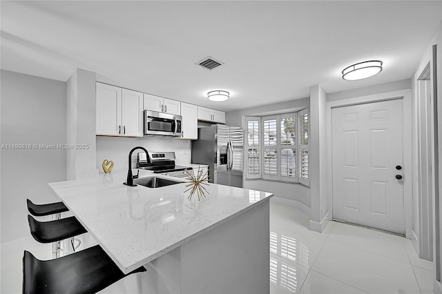 kitchen featuring a kitchen bar, white cabinetry, kitchen peninsula, stainless steel appliances, and light stone countertops