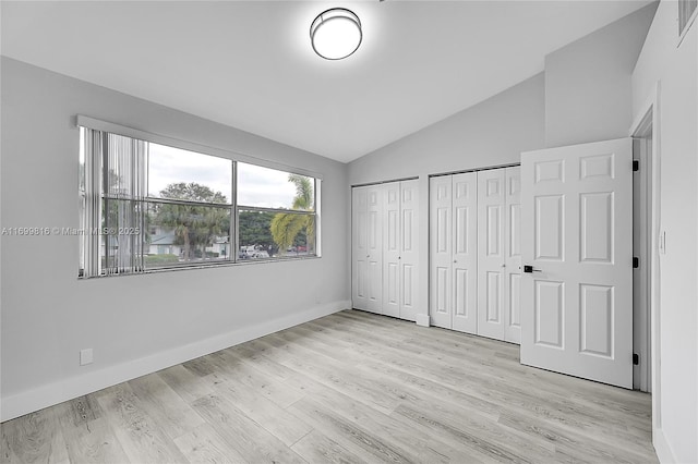 unfurnished bedroom featuring multiple closets, vaulted ceiling, and light hardwood / wood-style flooring