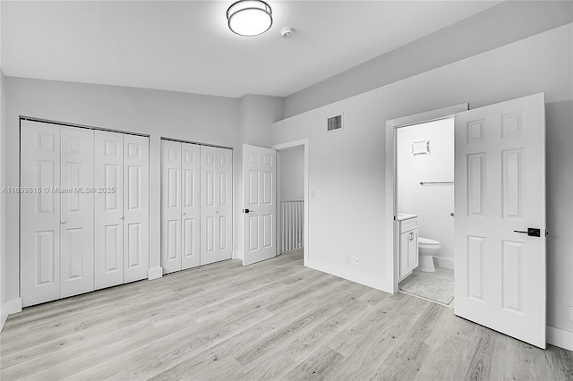 unfurnished bedroom featuring ensuite bath, vaulted ceiling, multiple closets, and light wood-type flooring