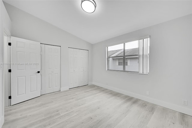 unfurnished bedroom featuring lofted ceiling, light hardwood / wood-style flooring, and two closets