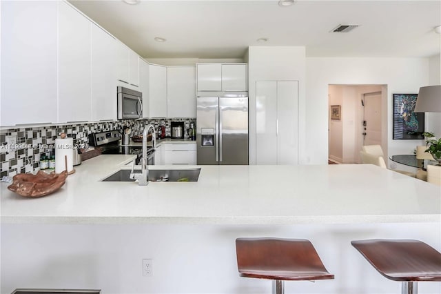 kitchen featuring backsplash, stainless steel appliances, white cabinetry, and a breakfast bar area