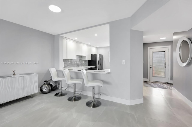 kitchen featuring white cabinetry, kitchen peninsula, stainless steel fridge, a breakfast bar area, and decorative backsplash