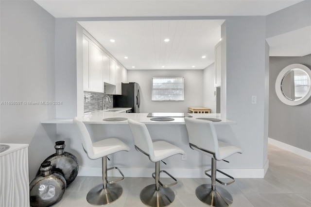 kitchen featuring kitchen peninsula, backsplash, sink, white cabinetry, and a breakfast bar area