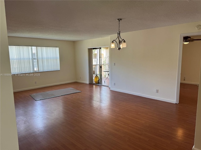 empty room with dark hardwood / wood-style floors, ceiling fan with notable chandelier, and a textured ceiling