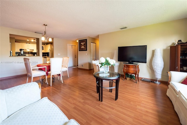 living room with light hardwood / wood-style flooring, a textured ceiling, and a notable chandelier