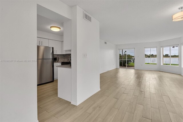 kitchen featuring stainless steel refrigerator, light hardwood / wood-style flooring, a textured ceiling, decorative backsplash, and white cabinets