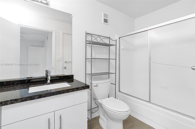 full bathroom with combined bath / shower with glass door, wood-type flooring, vanity, and toilet