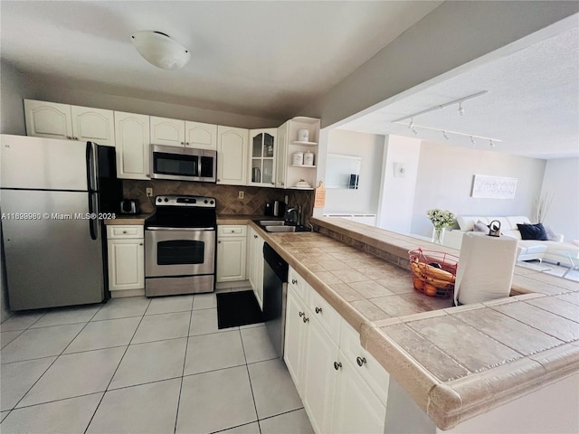 kitchen with appliances with stainless steel finishes, tasteful backsplash, sink, light tile patterned floors, and tile counters