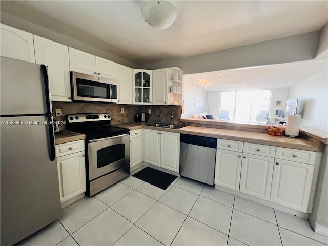 kitchen with sink, stainless steel appliances, light tile patterned floors, decorative backsplash, and white cabinets