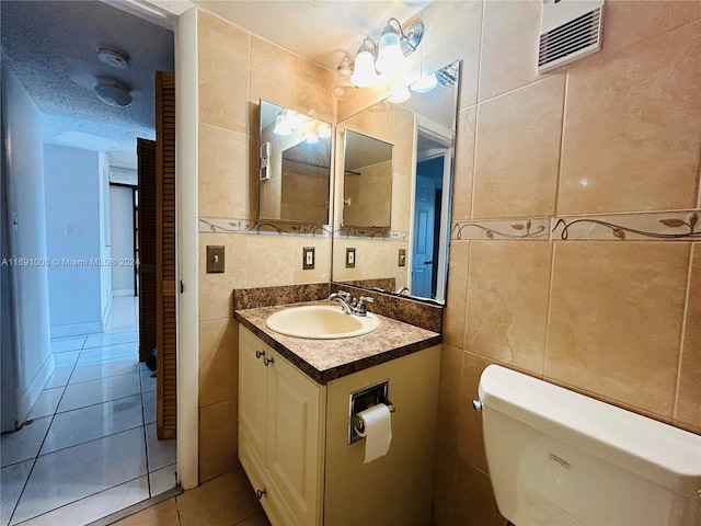 bathroom with tile patterned floors, a textured ceiling, toilet, vanity, and tile walls