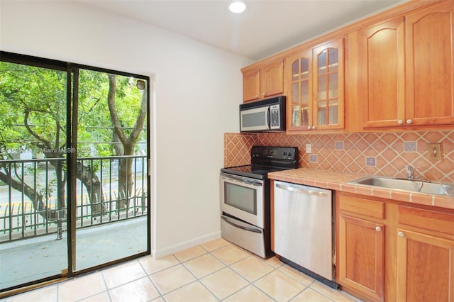 kitchen with tile countertops, light tile patterned floors, sink, and appliances with stainless steel finishes