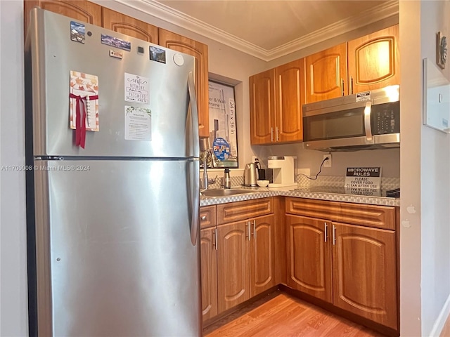 kitchen with appliances with stainless steel finishes, light hardwood / wood-style flooring, ornamental molding, and sink