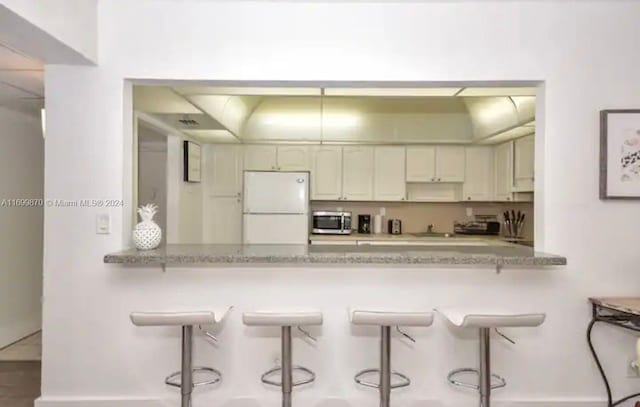 kitchen with kitchen peninsula, light stone counters, a breakfast bar, and white refrigerator