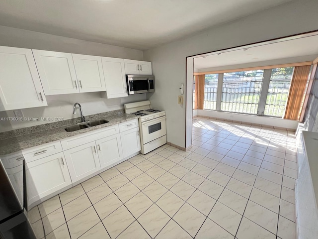 kitchen with white cabinets, sink, gas range gas stove, light tile patterned flooring, and light stone counters