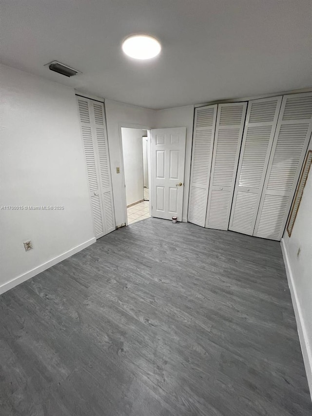 unfurnished bedroom featuring dark wood-type flooring and multiple closets