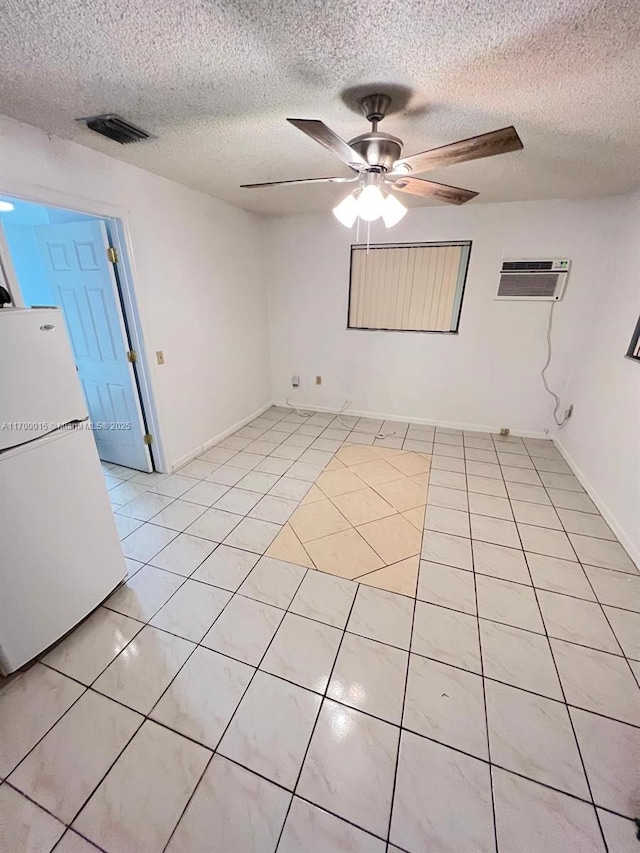 tiled empty room featuring a wall mounted air conditioner, ceiling fan, and a textured ceiling