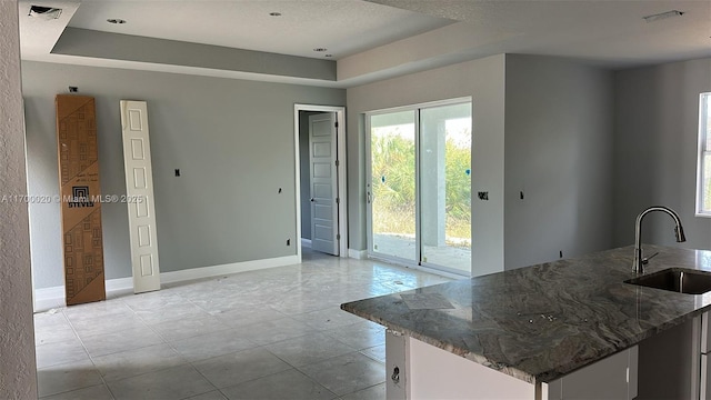 kitchen with white cabinets, a raised ceiling, dark stone counters, and sink