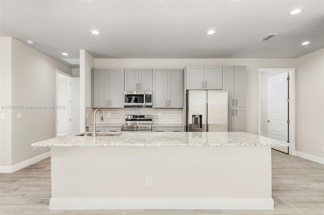 kitchen with sink, appliances with stainless steel finishes, an island with sink, and light stone counters