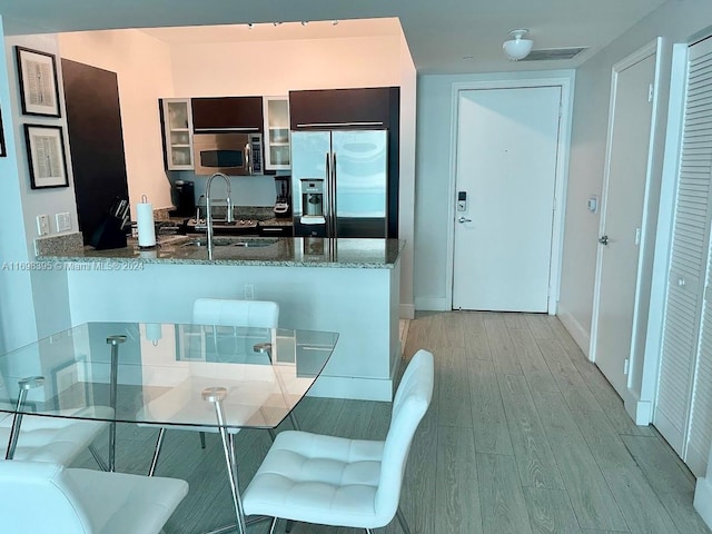 kitchen with stone counters, sink, stainless steel appliances, kitchen peninsula, and light wood-type flooring