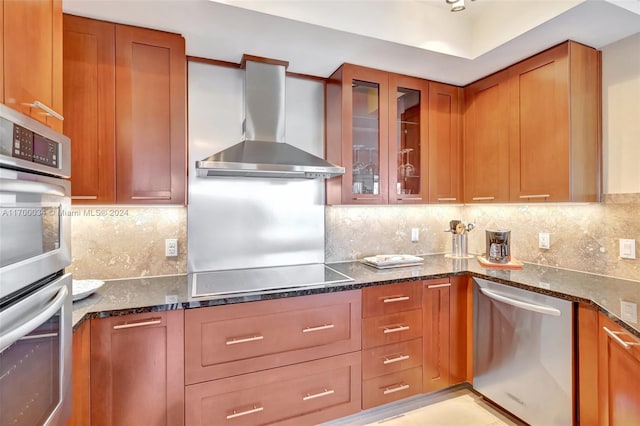 kitchen with decorative backsplash, appliances with stainless steel finishes, dark stone counters, and wall chimney range hood