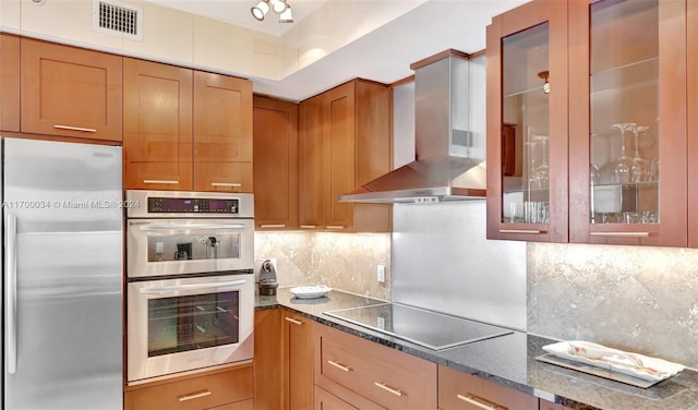 kitchen featuring wall chimney exhaust hood, backsplash, appliances with stainless steel finishes, and dark stone counters