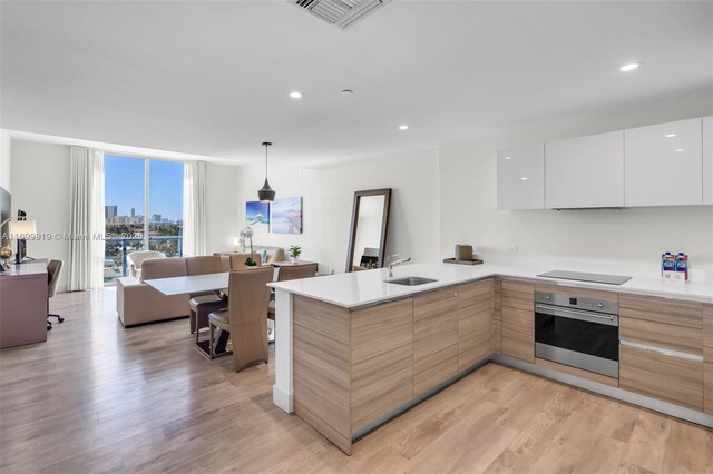 kitchen with sink, light hardwood / wood-style flooring, oven, pendant lighting, and white cabinets