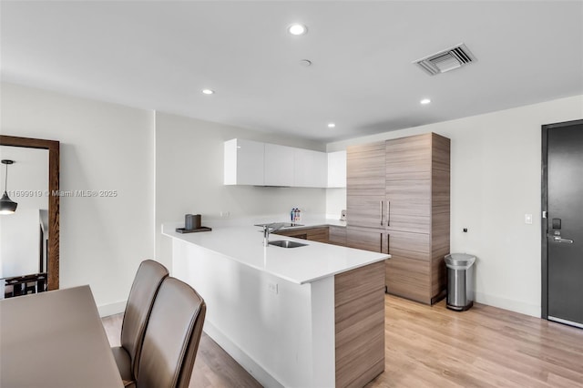 kitchen with white cabinetry, kitchen peninsula, sink, and light wood-type flooring