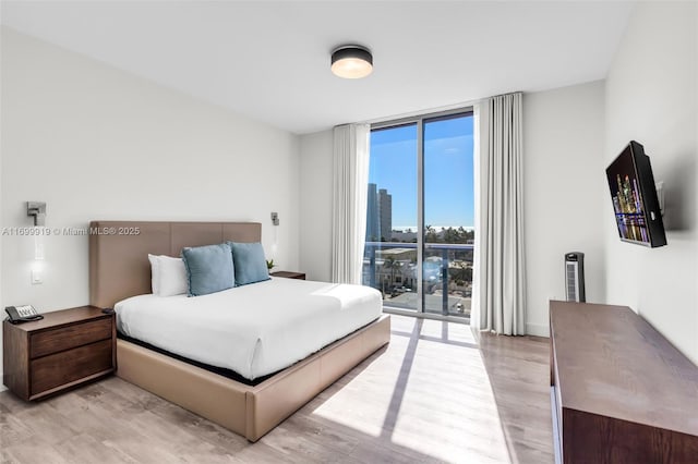 bedroom with a wall of windows, access to outside, and light hardwood / wood-style floors