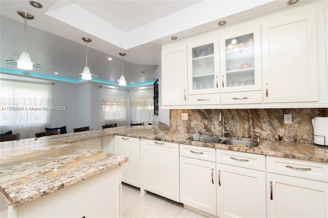 kitchen with sink, kitchen peninsula, decorative light fixtures, a tray ceiling, and white cabinets