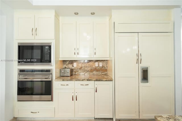 kitchen featuring decorative backsplash, built in appliances, stone countertops, and white cabinetry