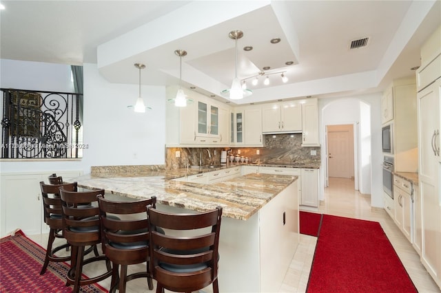 kitchen with backsplash, kitchen peninsula, pendant lighting, a tray ceiling, and white cabinets