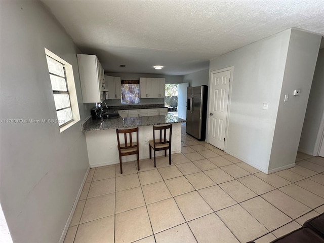 kitchen with stainless steel fridge with ice dispenser, light tile patterned floors, kitchen peninsula, and a wealth of natural light